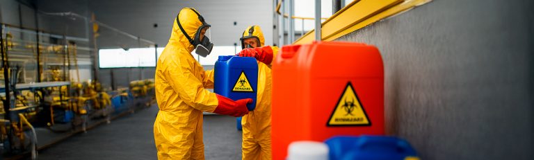 Trabalhador manuseando tambores de resíduos industriais com luvas e capacete.