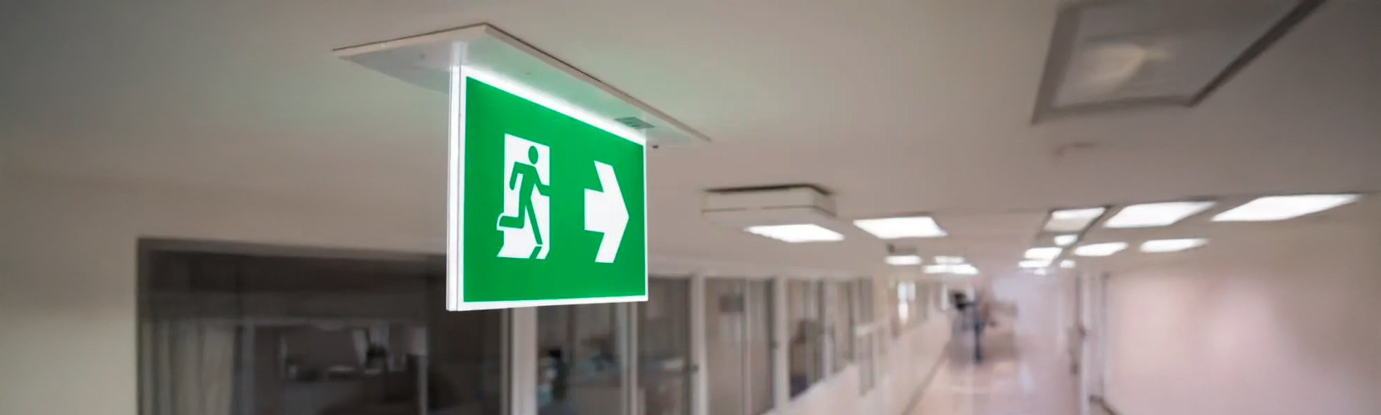 Placa de saída de emergência iluminada em corredor industrial.