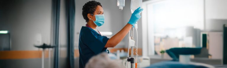 Enfermeira prestando atendimento a paciente hospitalizado com máscara e estetoscópio.
