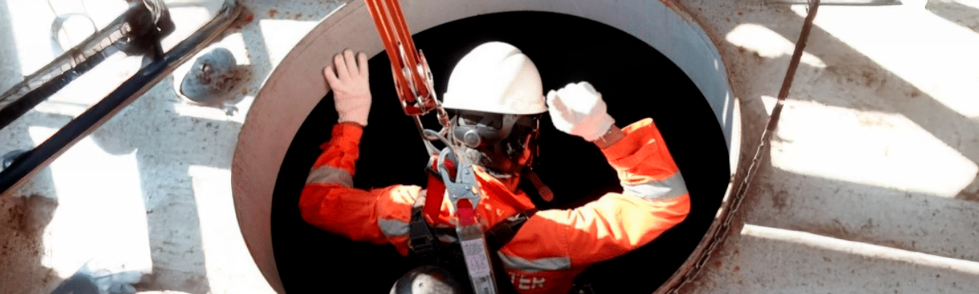 Trabalhador acessando espaço confinado com cinto de ancoragem, capacete e máscara.